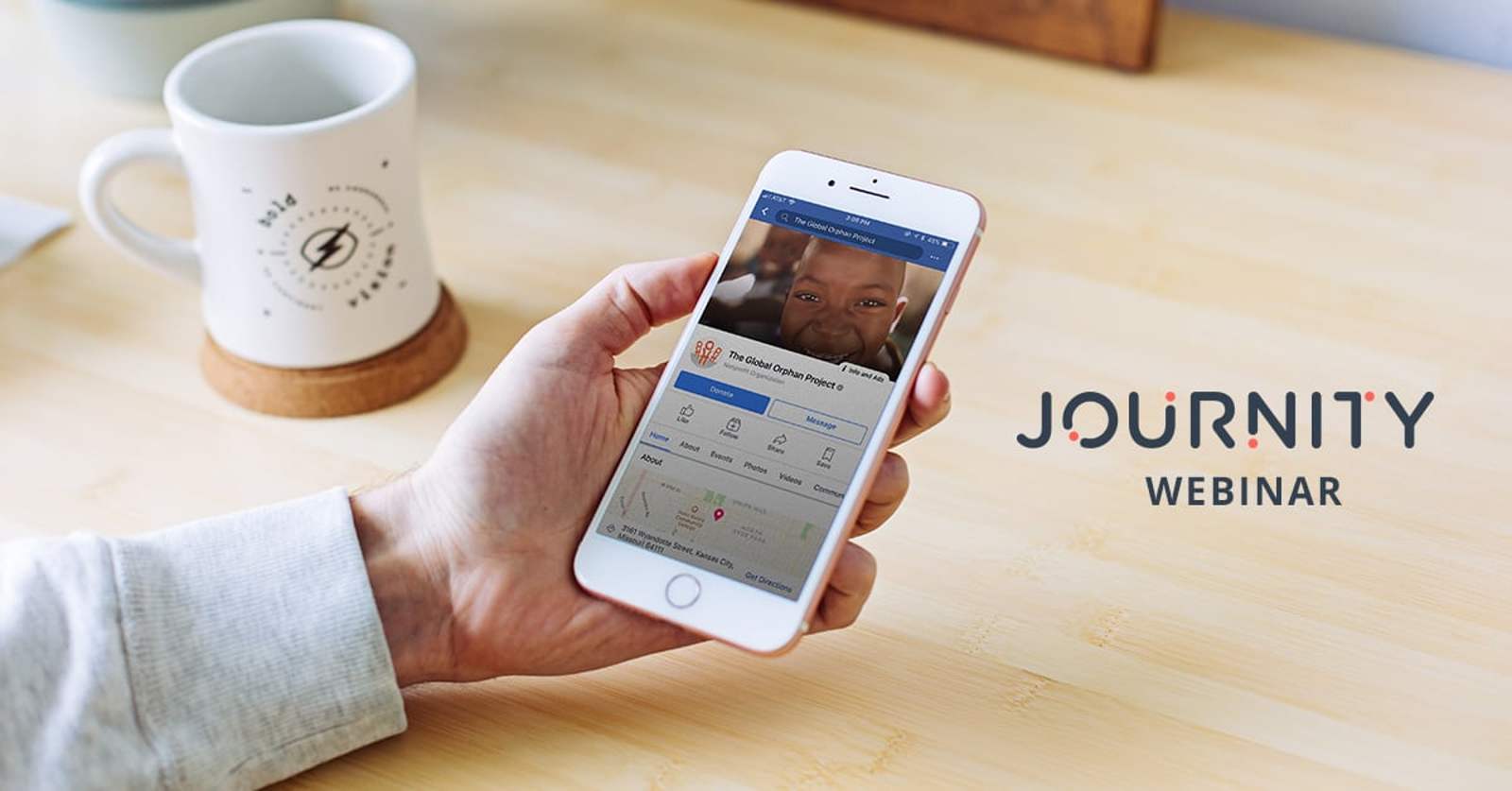 A hand holds a phone showing a Facebook page next to a coffee mug, with the Journity Webinar logo