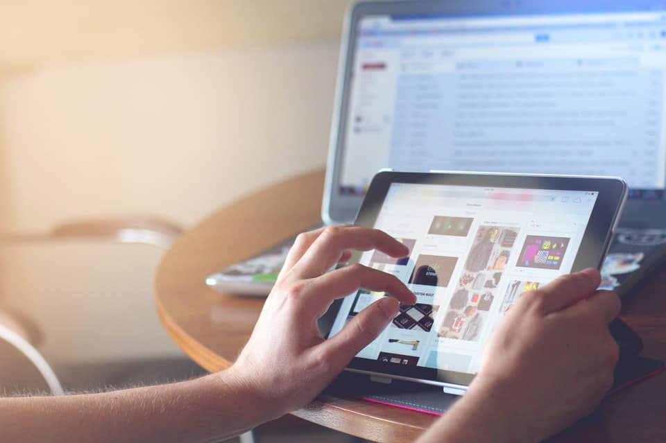 Hands browsing a shopping site on a tablet in front of an open laptop
