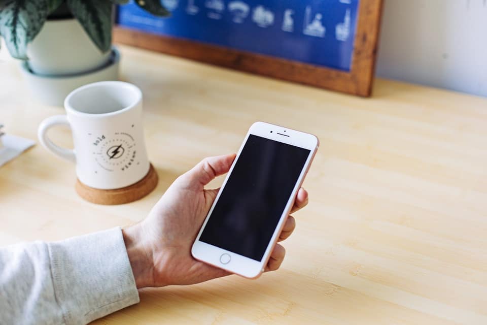 Hand holding a smartphone over a wooden desk next to a coffee mug