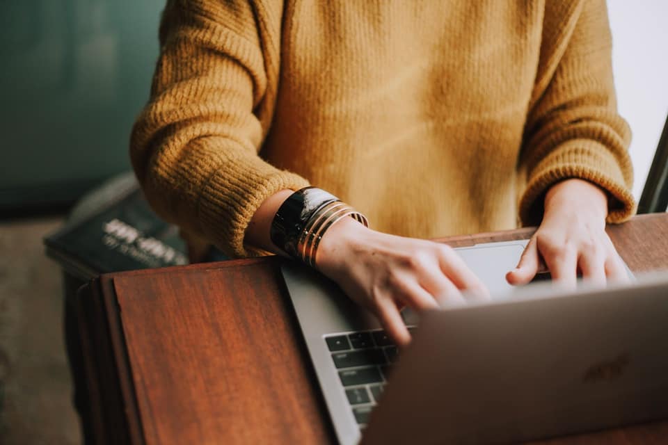 Person in a mustard sweater typing on a laptop