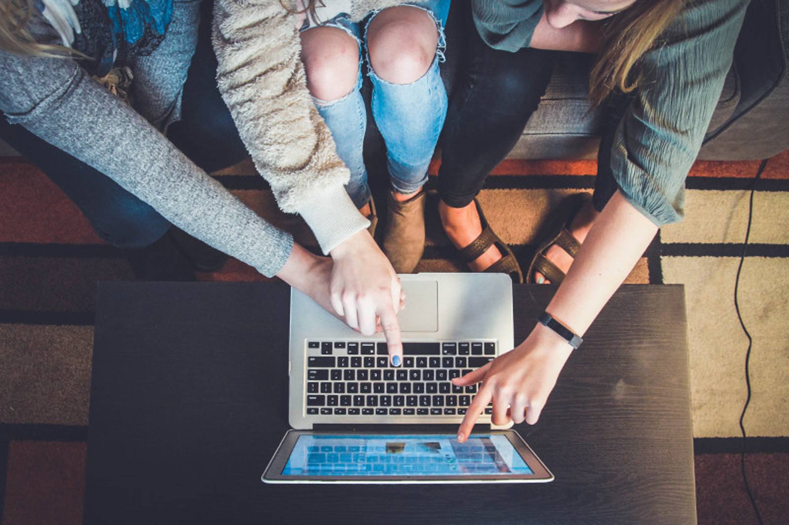 Three people on a couch pointing at a laptop screen together