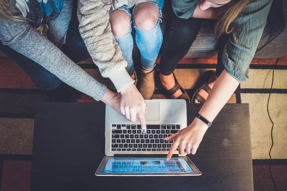 Three people on a couch pointing at a laptop screen together