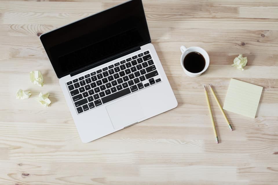 Laptop, cup of coffee, pencils, and sticky notes on a light wooden desk