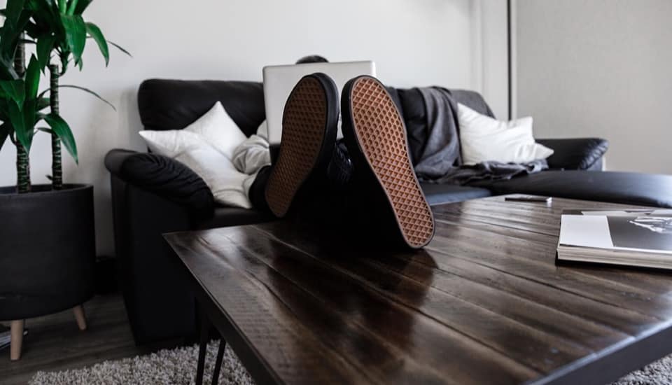 Person working on a laptop on a couch with feet up on a wooden coffee table